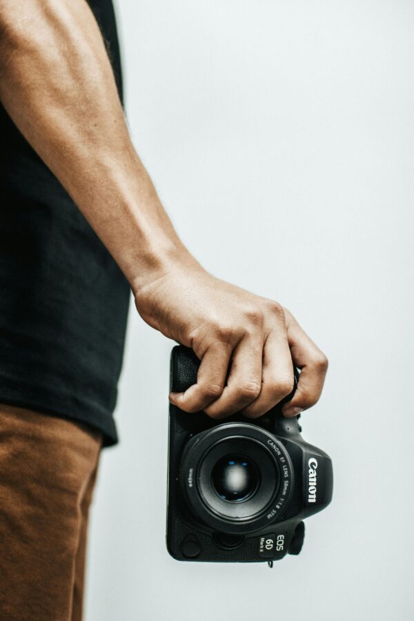 Close-up of a man holding a DSLR camera, focusing on the lens and grip.